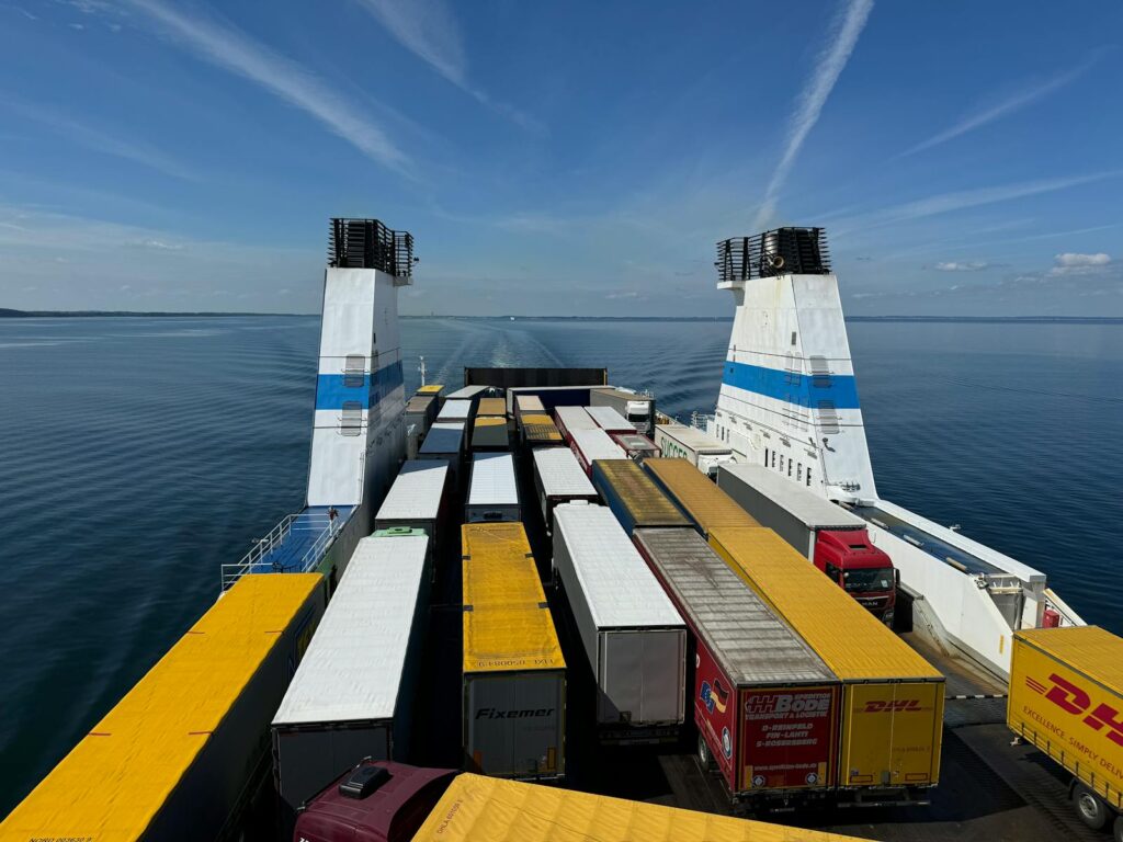 Überseeumzug mit Qualität | internationale & weltweite Umzugsspedition seit 30 Jahren 1 Aerial view of container trucks transported on a large ferry across a calm ocean under a clear blue sky.