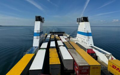 Aerial view of container trucks transported on a large ferry across a calm ocean under a clear blue sky.